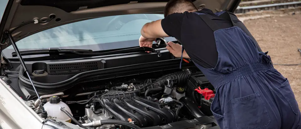 A technician leaning over the front of a silver SUV
